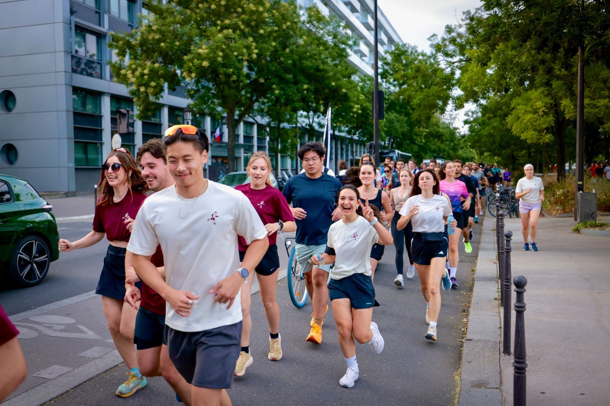 Des coureurs du club, souriants, en t-shirts bordeaux et crème au logo du Paris 11 Running Club, courent en groupe vers l'objectif dans une rue arborée